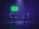 Dos sillas enfrentadas bajo un foco con un bocadillo de diálogo verde luminoso: la entrevista de trabajo en inglés